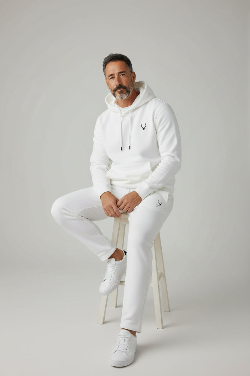 Man wearing a white hoodie and pants sitting on a stool against a gray background. Antler, Monza Outlet, Monza Fashion, Shein Outlet
