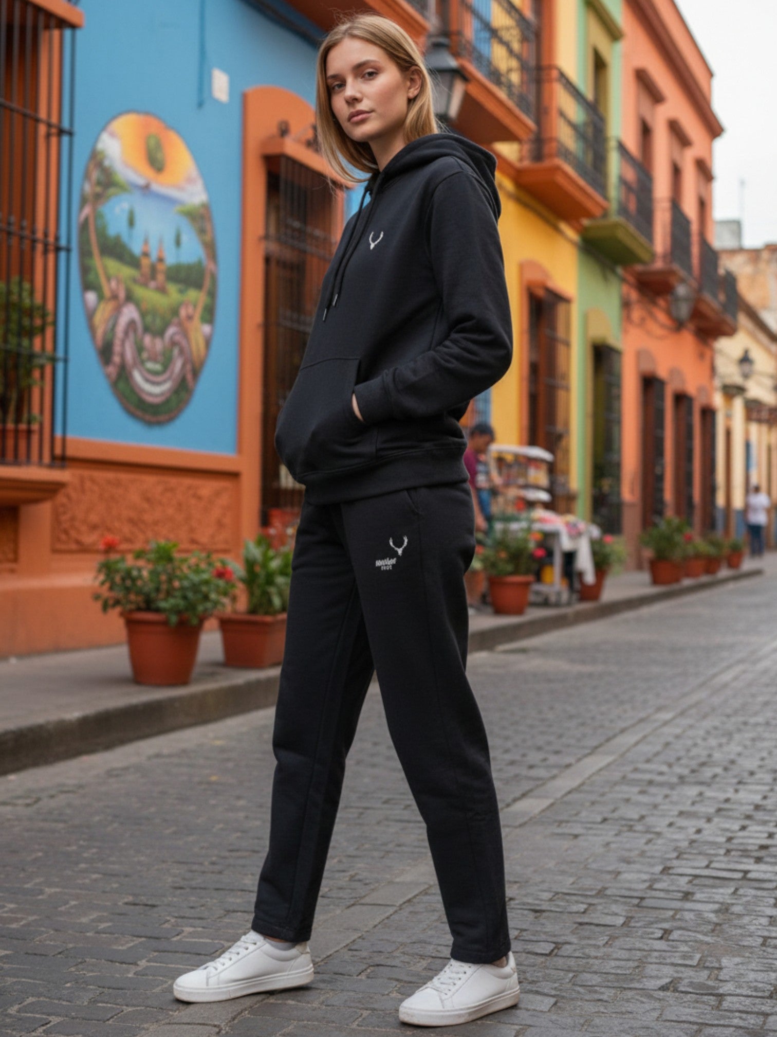 Person wearing a black hoodie and pants on a colorful street. Antler, Monza Outlet, Monza Fashion, Shein Outlet
