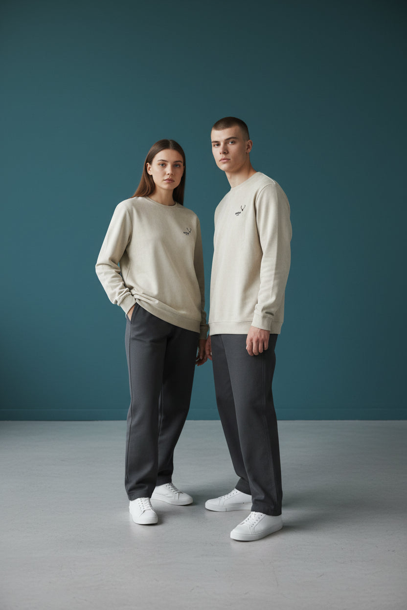 Two people wearing matching beige long-sleeve shirts and dark pants against a teal background. Antler, Monza Outlet, Monza Fashion, Shein Outlet