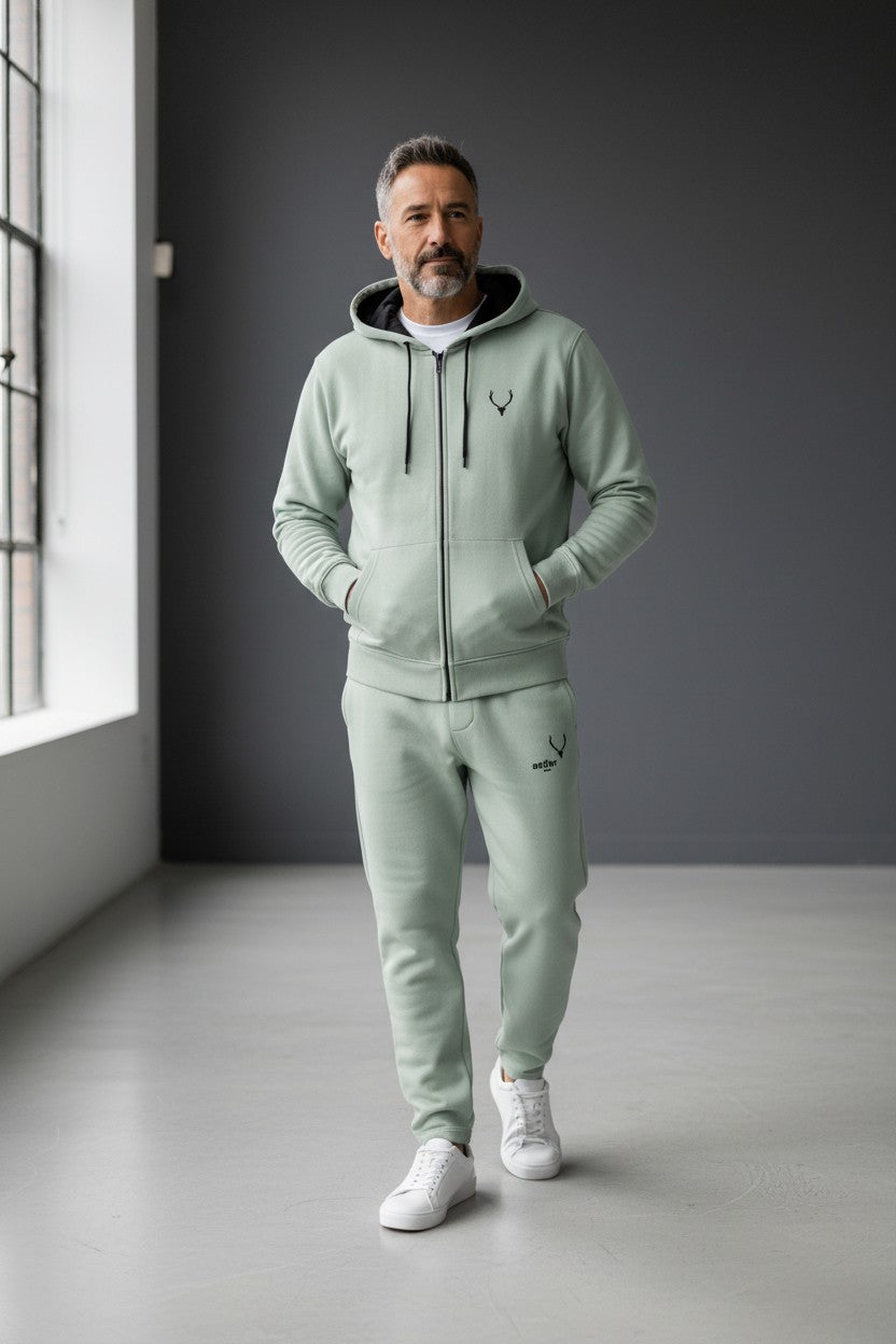 Man wearing a light green tracksuit with a logo in a room with a window and gray walls. Antler, Monza Outlet, Monza Fashion, Shein Outlet