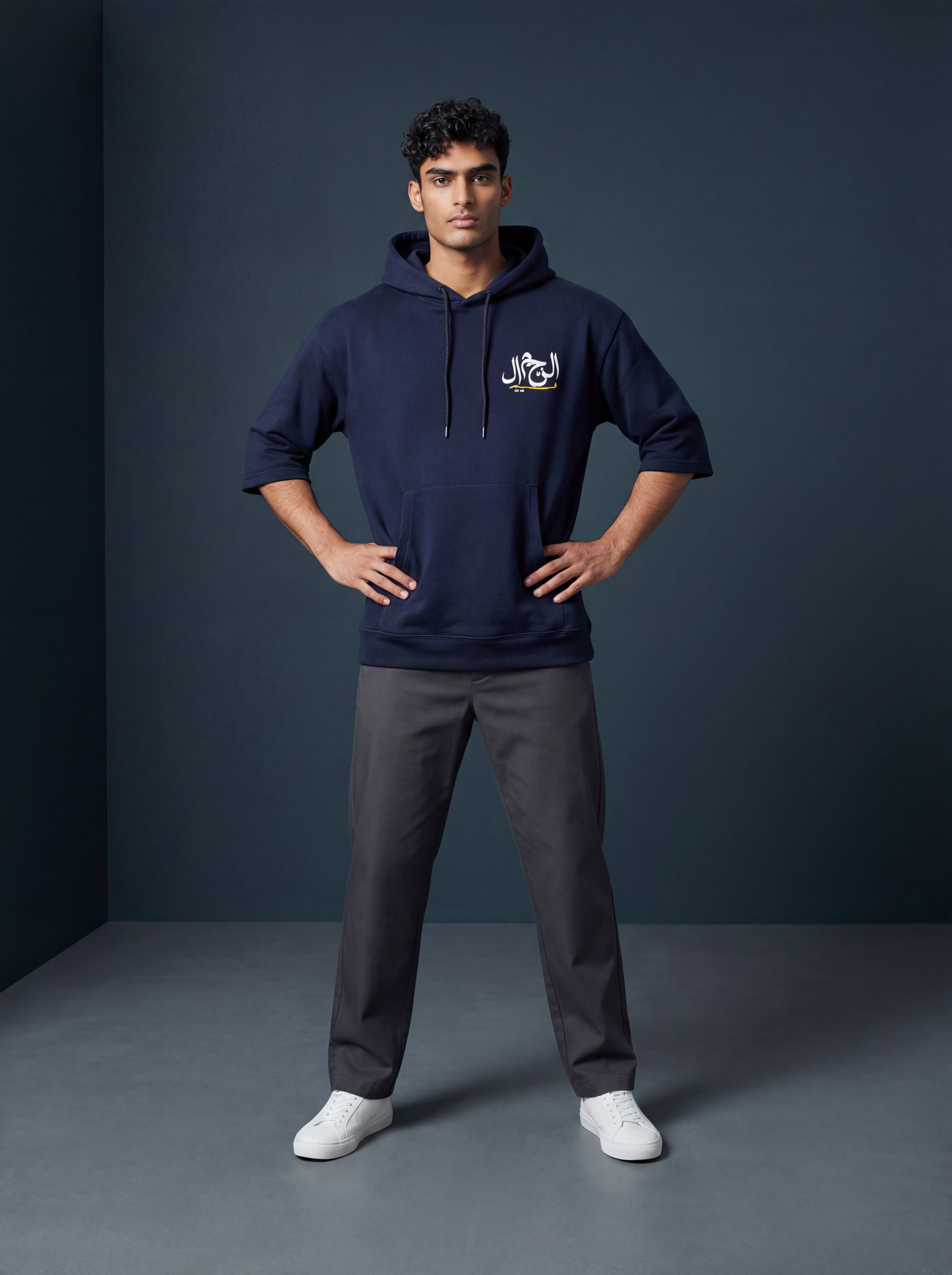 Man wearing a navy hoodie with a logo and gray pants against a dark background. Antler, Monza Outlet, Monza Fashion, Shein Outlet