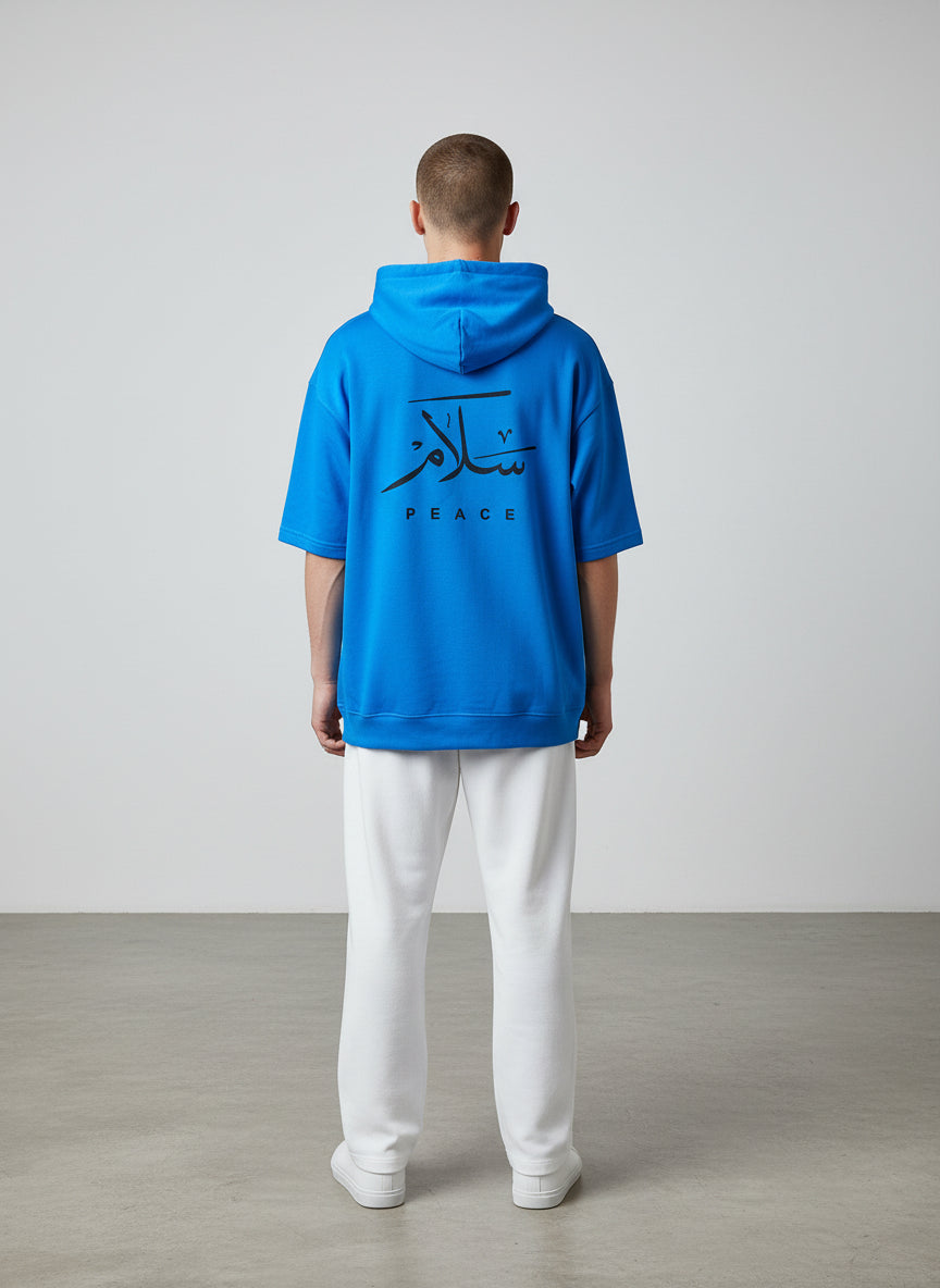 Person wearing a blue hoodie with Arabic text and 'PEACE' on the back, standing against a plain background. Antler, Monza Outlet, Monza Fashion, Shein Outlet