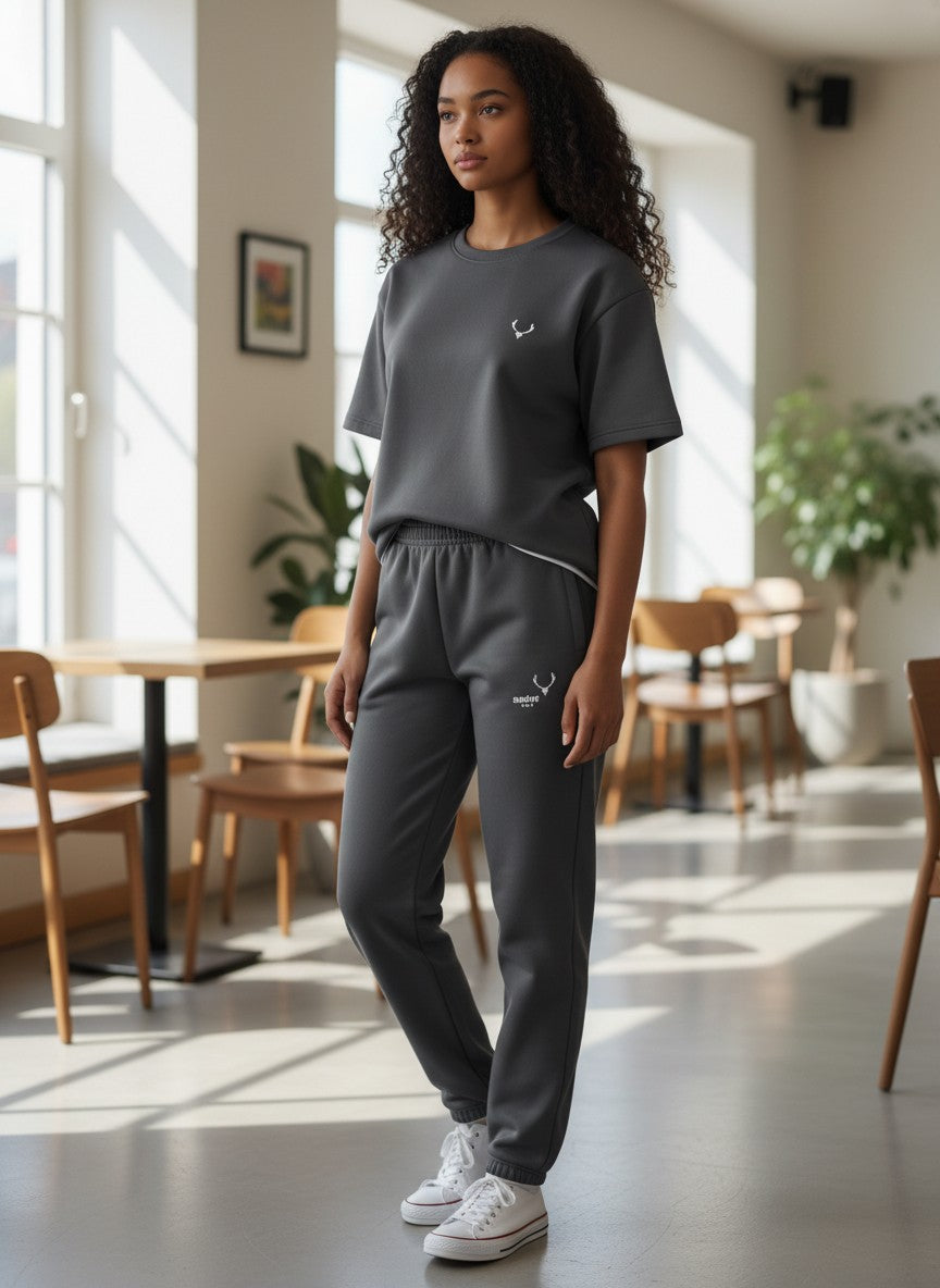 Person wearing a dark gray outfit with a logo in a bright room with wooden furniture and plants. Antler, Monza Outlet, Monza Fashion, Shein Outlet
