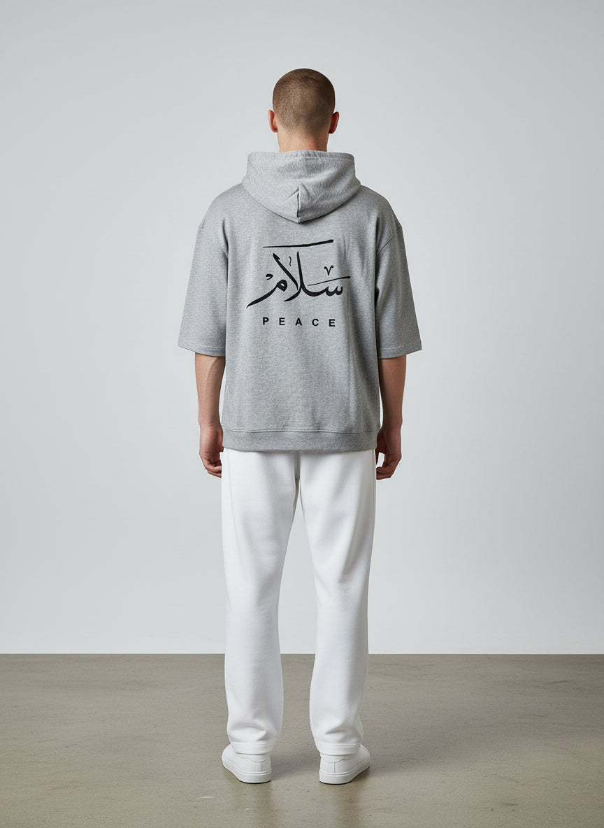 Person wearing a gray hoodie with Arabic text and 'PEACE' on the back, standing against a plain background. Antler, Monza Outlet, Monza Fashion, Shein Outlet
