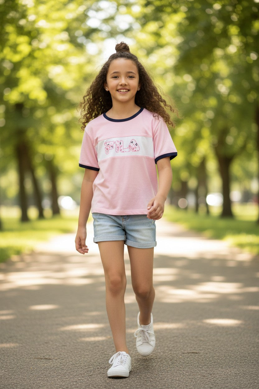 Young girl in a pink shirt and denim shorts walking on a path with trees in the background. Fila, Monza Outlet, Monza Fashion, Shein Outlet