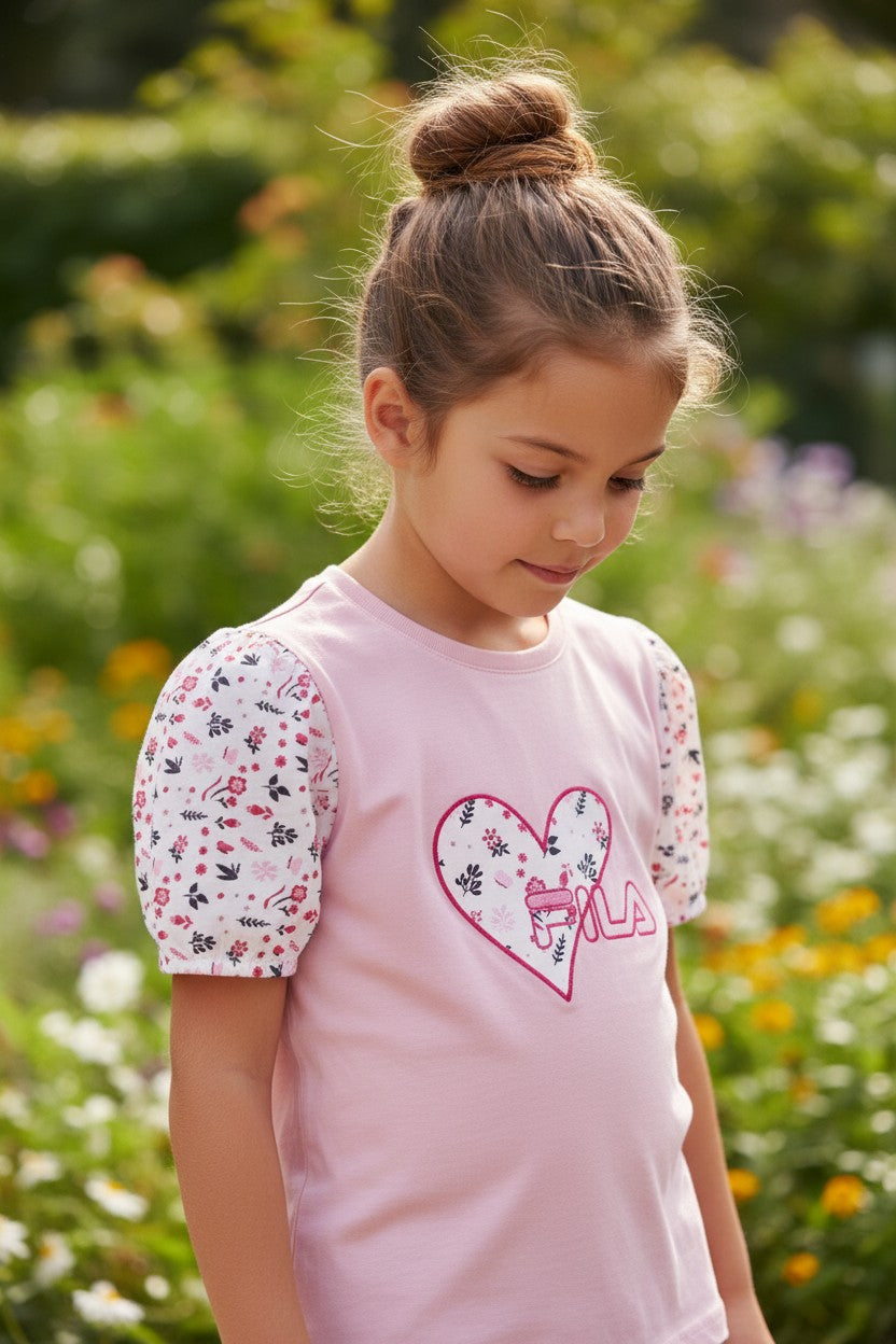 Young girl wearing a pink shirt with a heart design in a garden setting. Fila, Monza Outlet, Monza Fashion, Shein Outlet