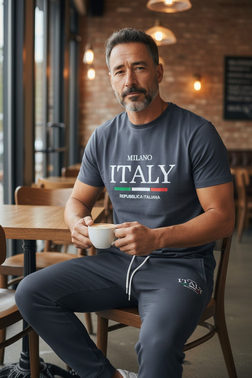 Man sitting in a cafe holding a cup, wearing a Milano Italy t-shirt. Antler, Monza Outlet, Monza Fashion, Shein Outlet