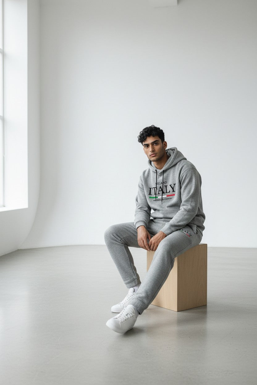 Person wearing a gray hoodie with ITALY text sitting on a box in a minimalistic room. Antler, Monza Outlet, Monza Fashion, Shein Outlet