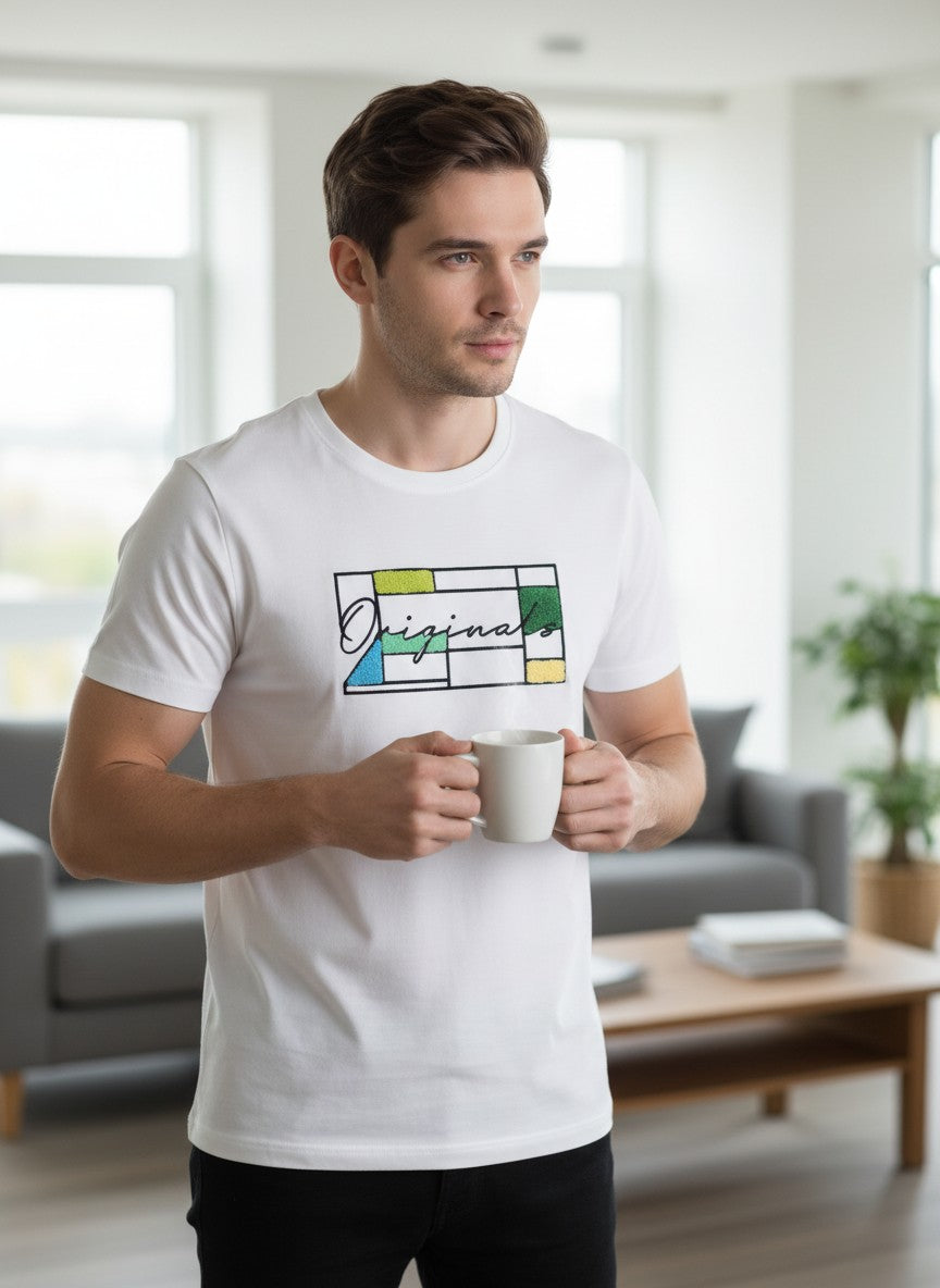 Man wearing a white t-shirt with a colorful design, holding a mug in a living room. Jack & Jones, Monza Outlet, Monza Fashion, Shein Outlet