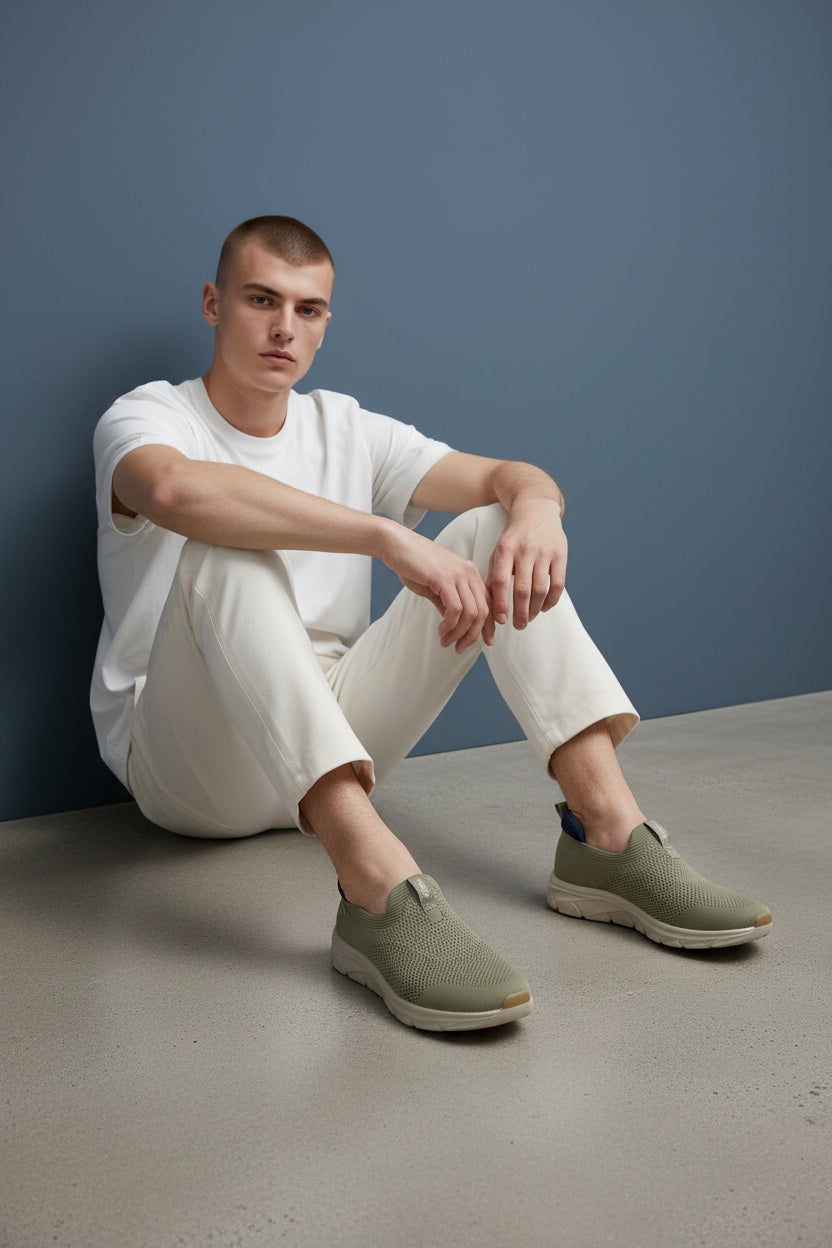 Man wearing a white t-shirt and light-colored pants with green shoes against a blue wall. Maklinit, Monza Outlet, Monza Fashion, Shein Outlet