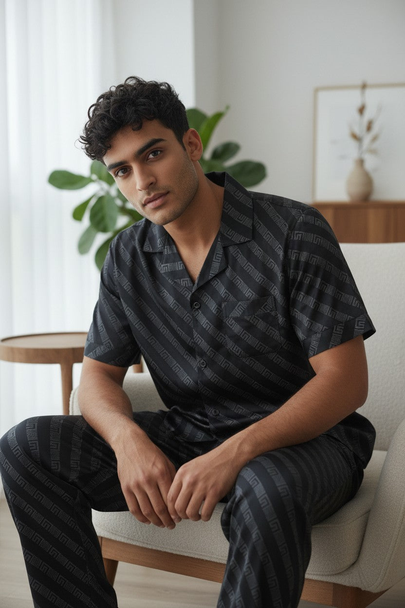 Man wearing a black striped shirt and pants sitting on a white chair in a bright room. Monza Italy, Monza Outlet, Monza Fashion, Shein Outlet