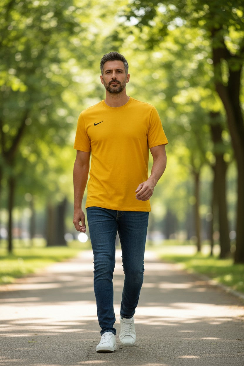 Man walking on a path in a park wearing a yellow Nike t-shirt and blue jeans. Nike, Monza Outlet, Monza Fashion, Shein Outlet