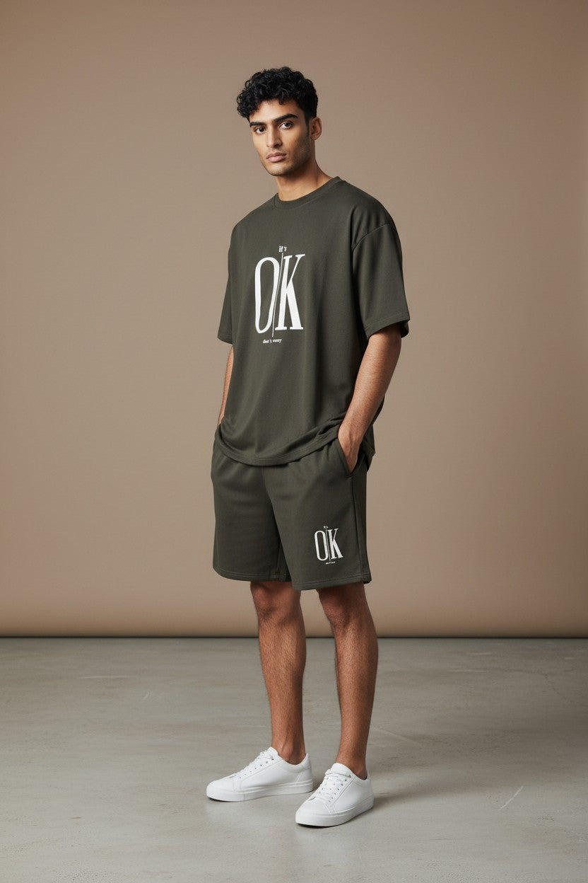 Man wearing a green OK t-shirt and shorts against a beige background. Antler, Monza Outlet, Monza Fashion, Shein Outlet