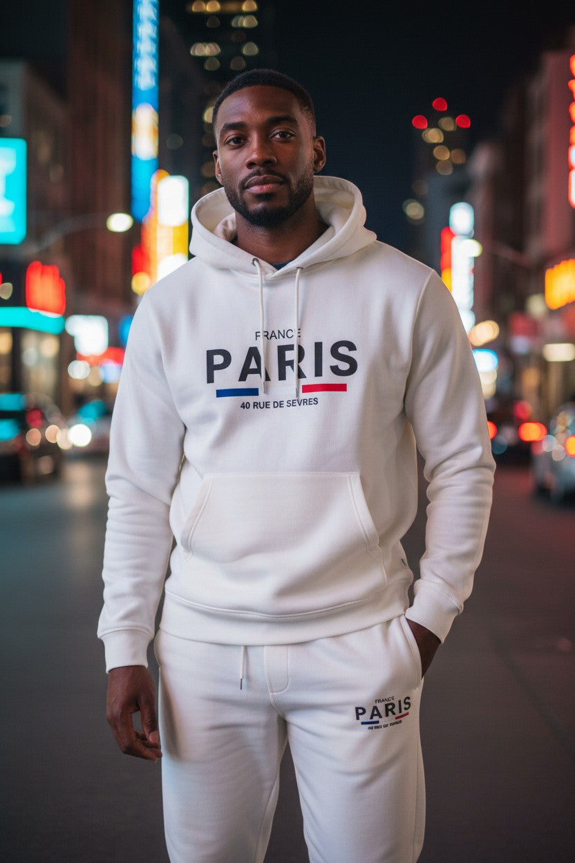 Man wearing a white hoodie and pants with Paris text on a city street at night. Antler, Monza Outlet, Monza Fashion, Shein Outlet