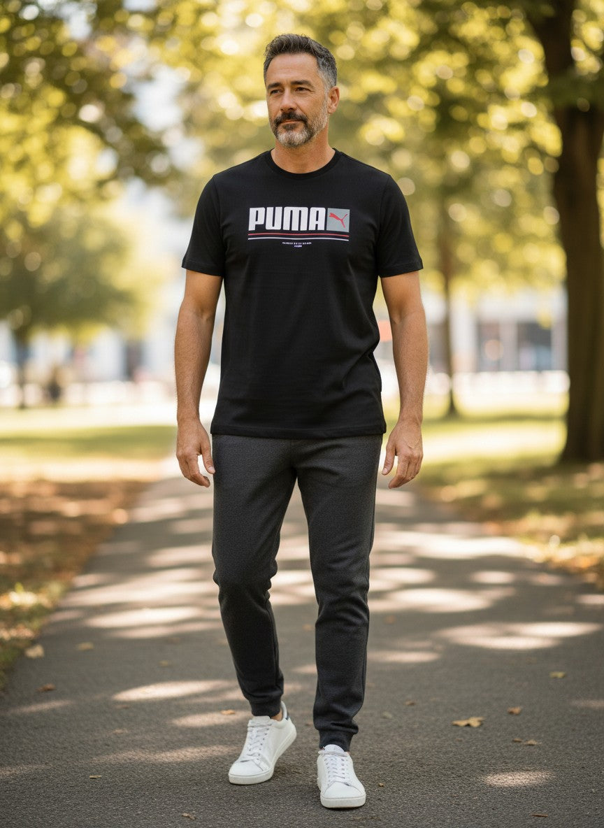 Man wearing a black Puma t-shirt and dark pants walking on a path with trees in the background. Puma, Monza Outlet, Monza Fashion, Shein Outlet