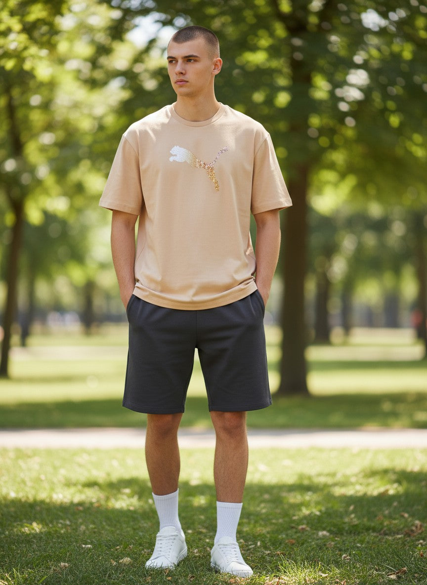 Person wearing a beige t-shirt and dark shorts standing in a park. Puma, Monza Outlet, Monza Fashion, Shein Outlet