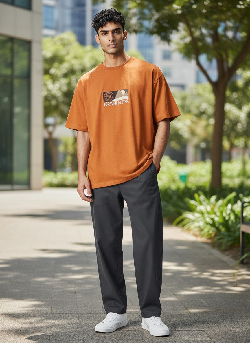 Man wearing an orange t-shirt with a graphic design, dark pants, and white shoes standing outdoors. Puma, Monza Outlet, Monza Fashion, Shein Outlet