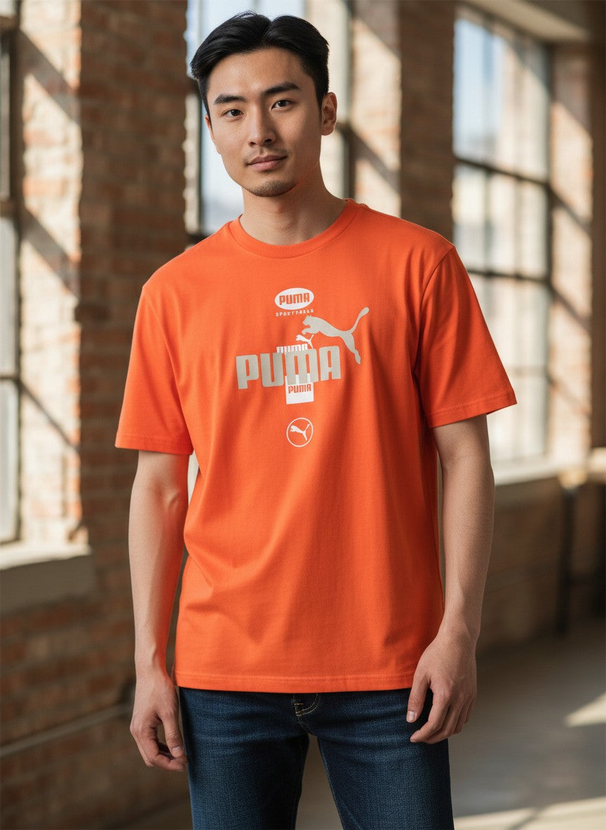 Person wearing an orange Puma t-shirt standing in a sunlit room with brick walls. Puma, Monza Outlet, Monza Fashion, Shein Outlet