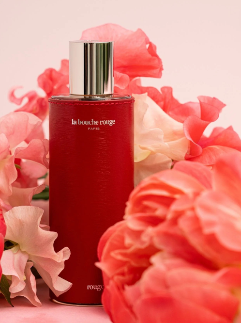 Red bottle of la bouche rouge with pink flowers in the background La Bouche Rouge Monza Outlet
