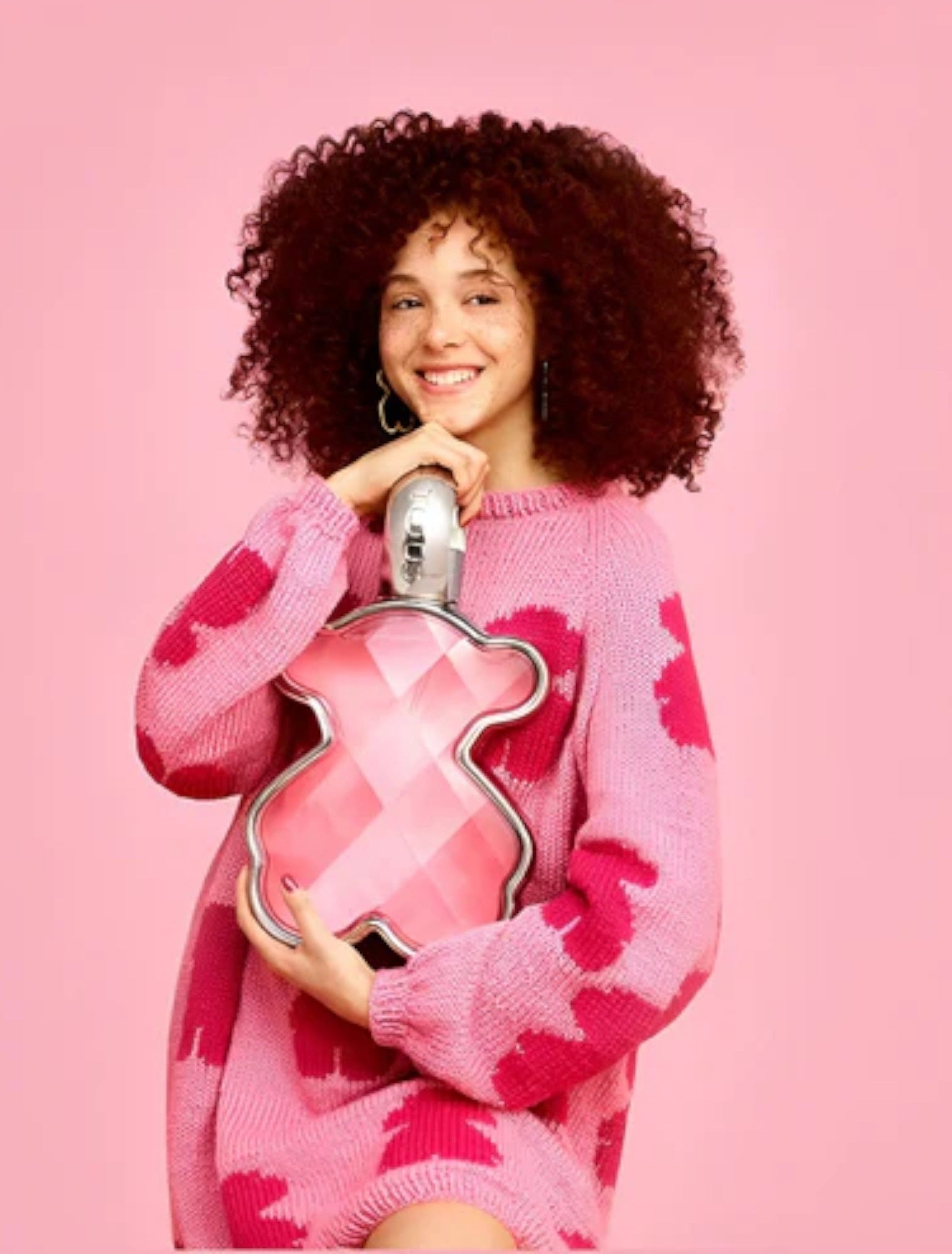 Person holding a pink and silver bottle against a pink background. Tous Love Me, Monza Outlet, Monza Fashion, Shein Outlet