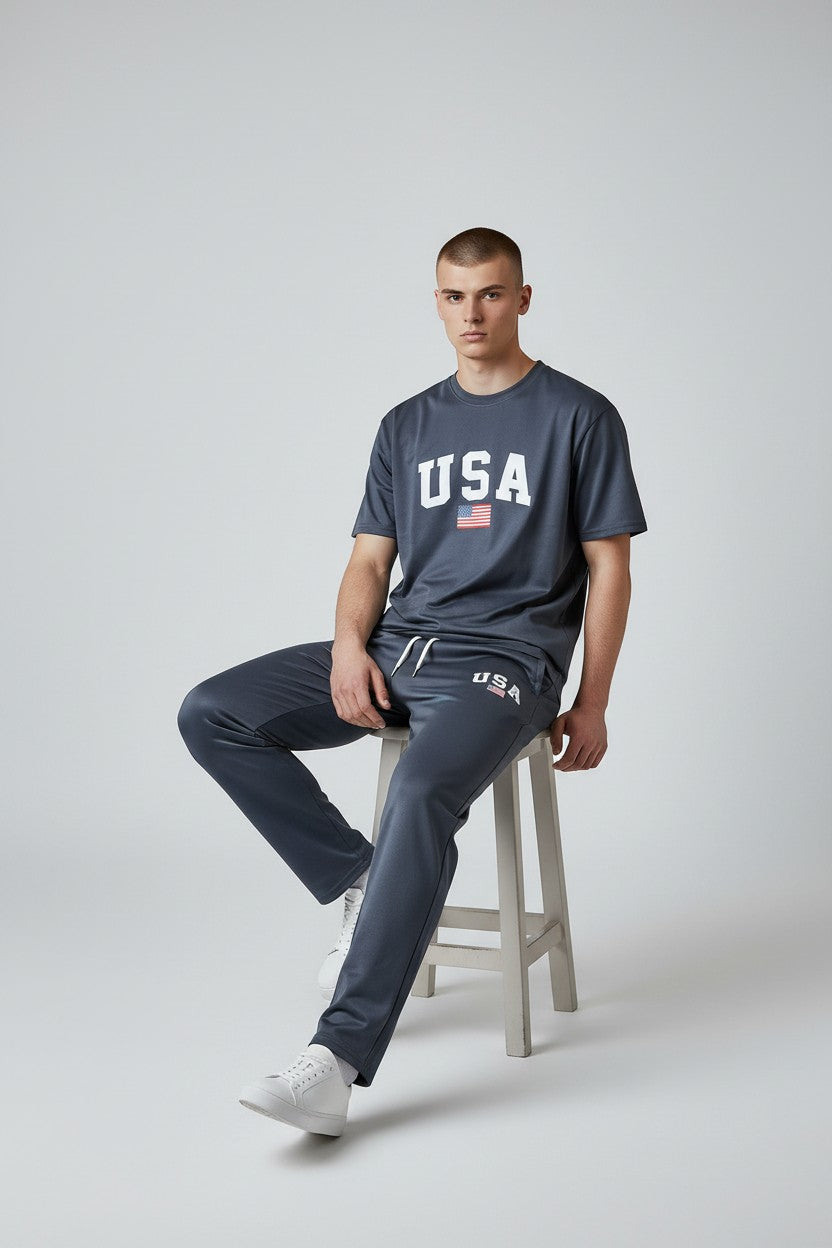 Person wearing a dark gray USA t-shirt and pants sitting on a stool against a plain background. Antler, Monza Outlet, Monza Fashion, Shein Outlet