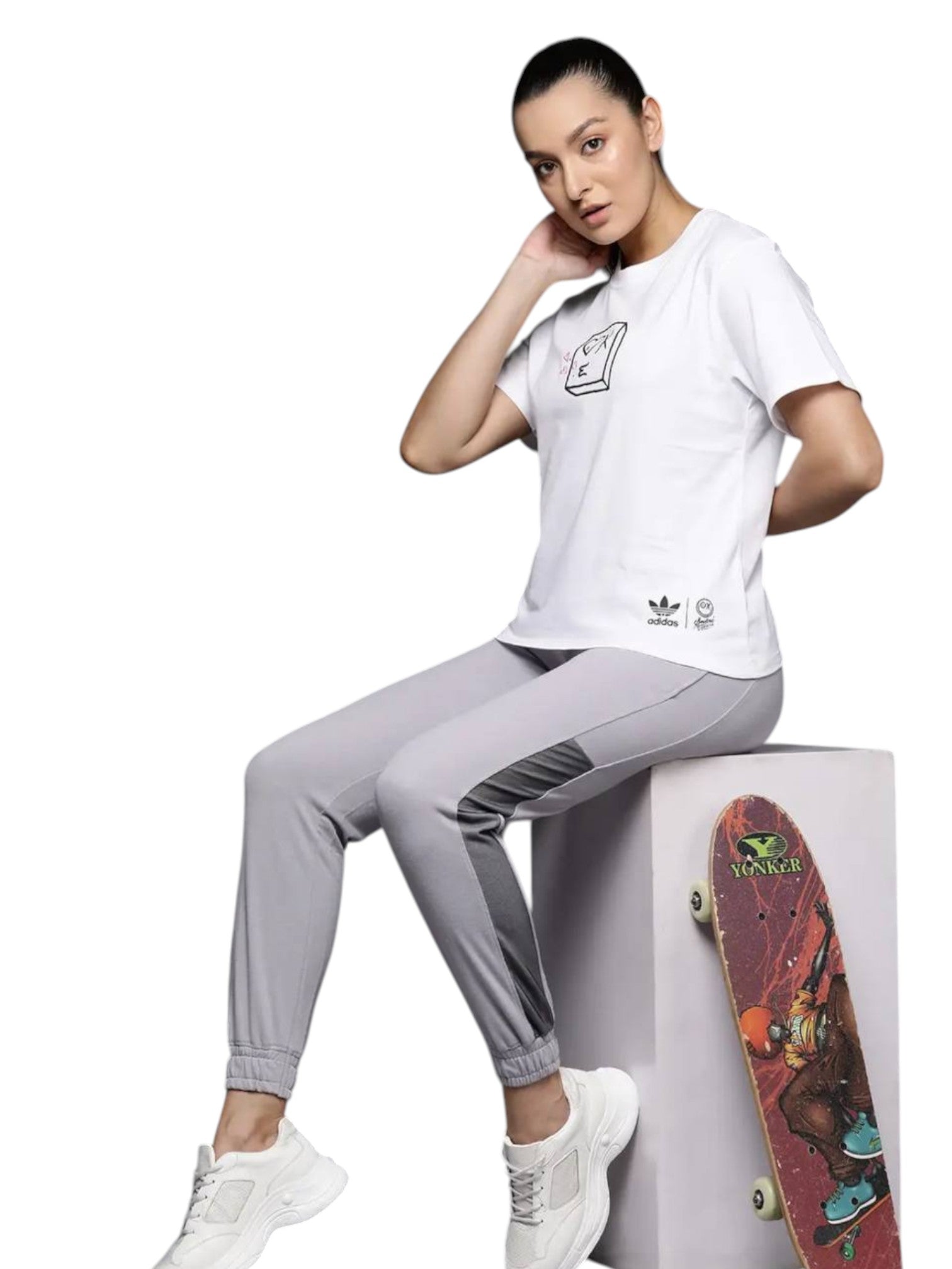 Person wearing a white Adidas t-shirt and gray pants sitting on a white block with a skateboard next to them. Adidas, Monza Outlet, Monza Fashion, Shein Outlet