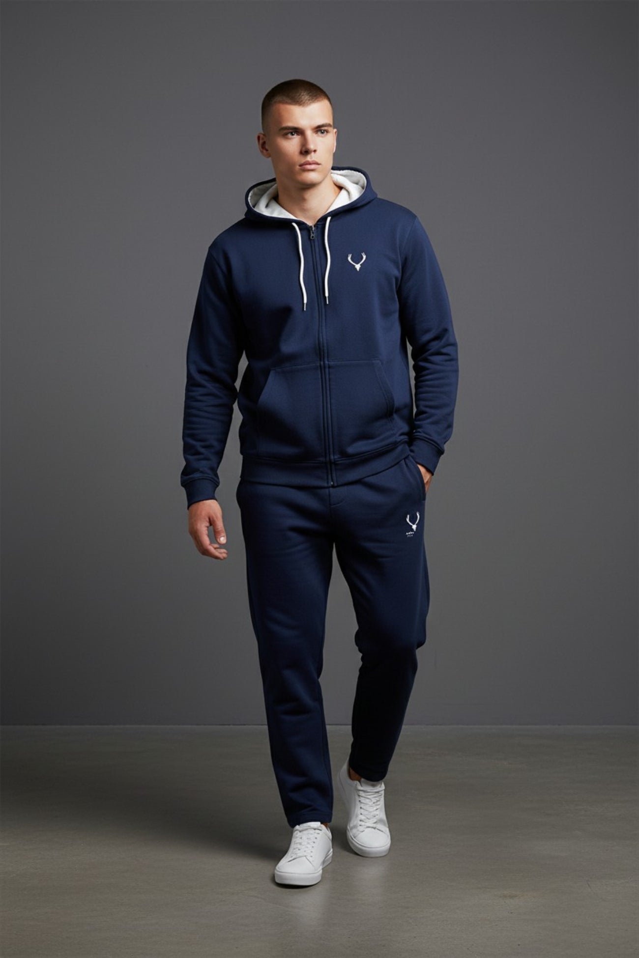 Man wearing a navy blue tracksuit with a logo on a gray background. Antler, Monza Outlet, Monza Fashion, Shein Outlet