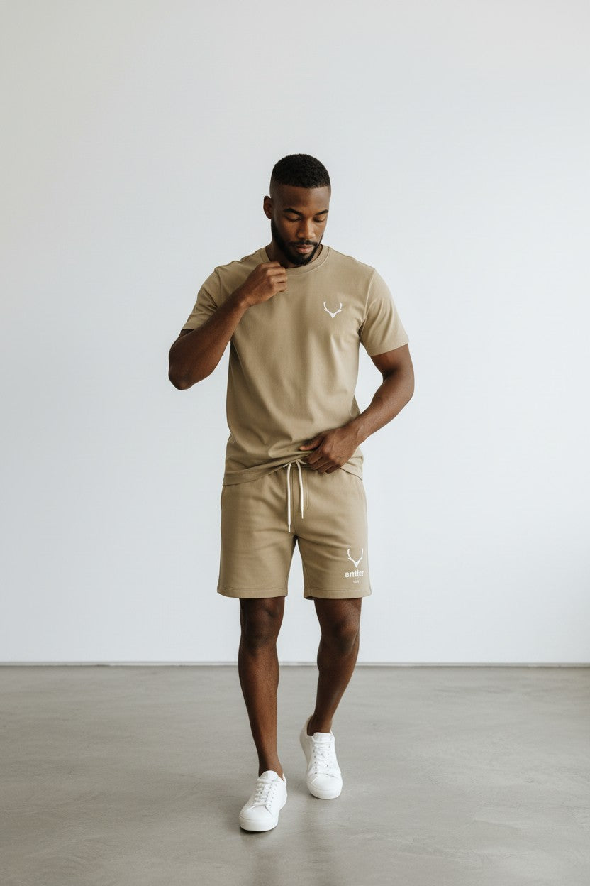 Man wearing a beige t-shirt and shorts set with white sneakers on a plain background. Antler, Monza Outlet, Monza Fashion, Shein Outlet