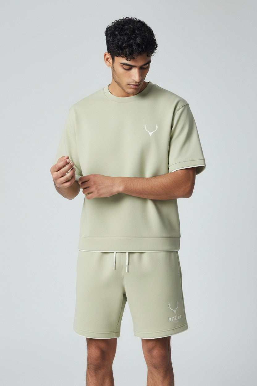 Man wearing a light green t-shirt and shorts with a logo on a plain background. Antler, Monza Outlet, Monza Fashion, Shein Outlet