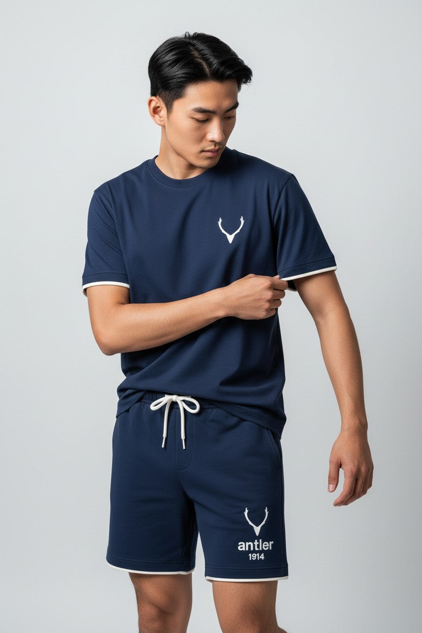 Person wearing a navy blue t-shirt and shorts set with a logo on a light gray background. Antler, Monza Outlet, Monza Fashion, Shein Outlet