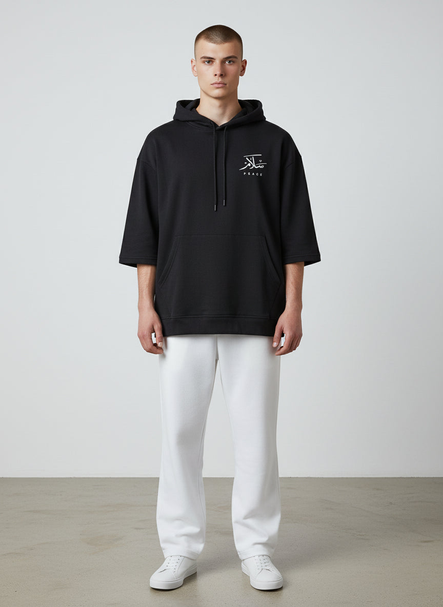 Person wearing a black hoodie with a logo and white pants on a light gray background. Antler, Monza Outlet, Monza Fashion, Shein Outlet