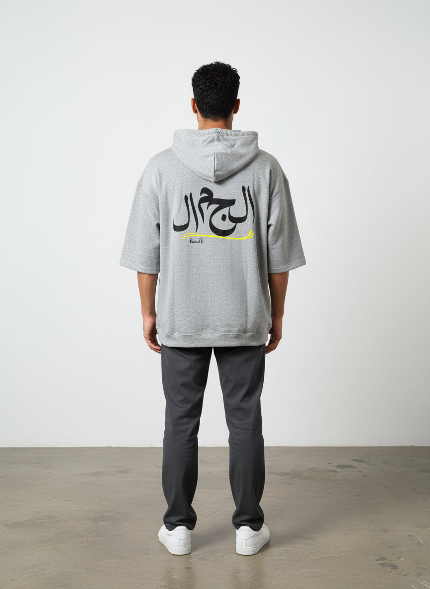 Person wearing a gray hoodie with Arabic text on the back, standing against a white wall. Antler, Monza Outlet, Monza Fashion, Shein Outlet