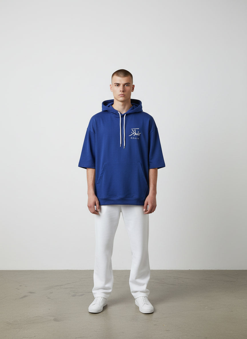 Man wearing a blue hoodie with a logo, white pants, and white shoes on a plain background. Antler, Monza Outlet, Monza Fashion, Shein Outlet