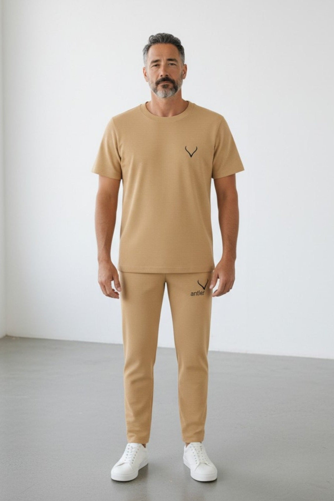Man wearing a beige t-shirt and pants with a logo, standing against a white background. Antler, Monza Outlet, Monza Fashion, Shein Outlet