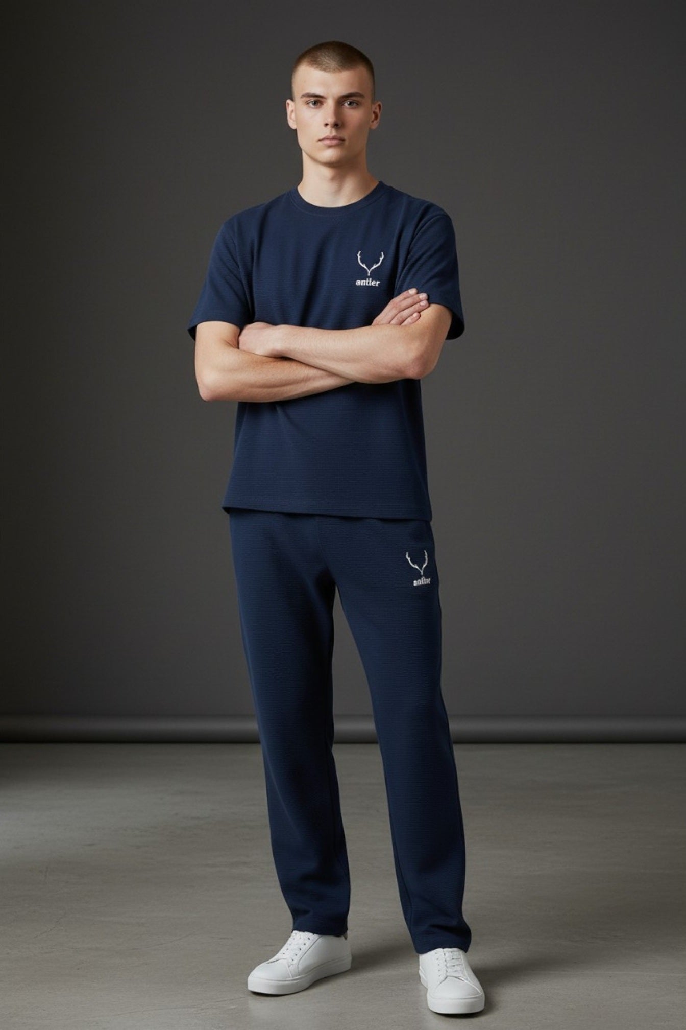 Man wearing navy blue t-shirt and pants with a logo, standing against a gray background. Antler, Monza Outlet, Monza Fashion, Shein Outlet