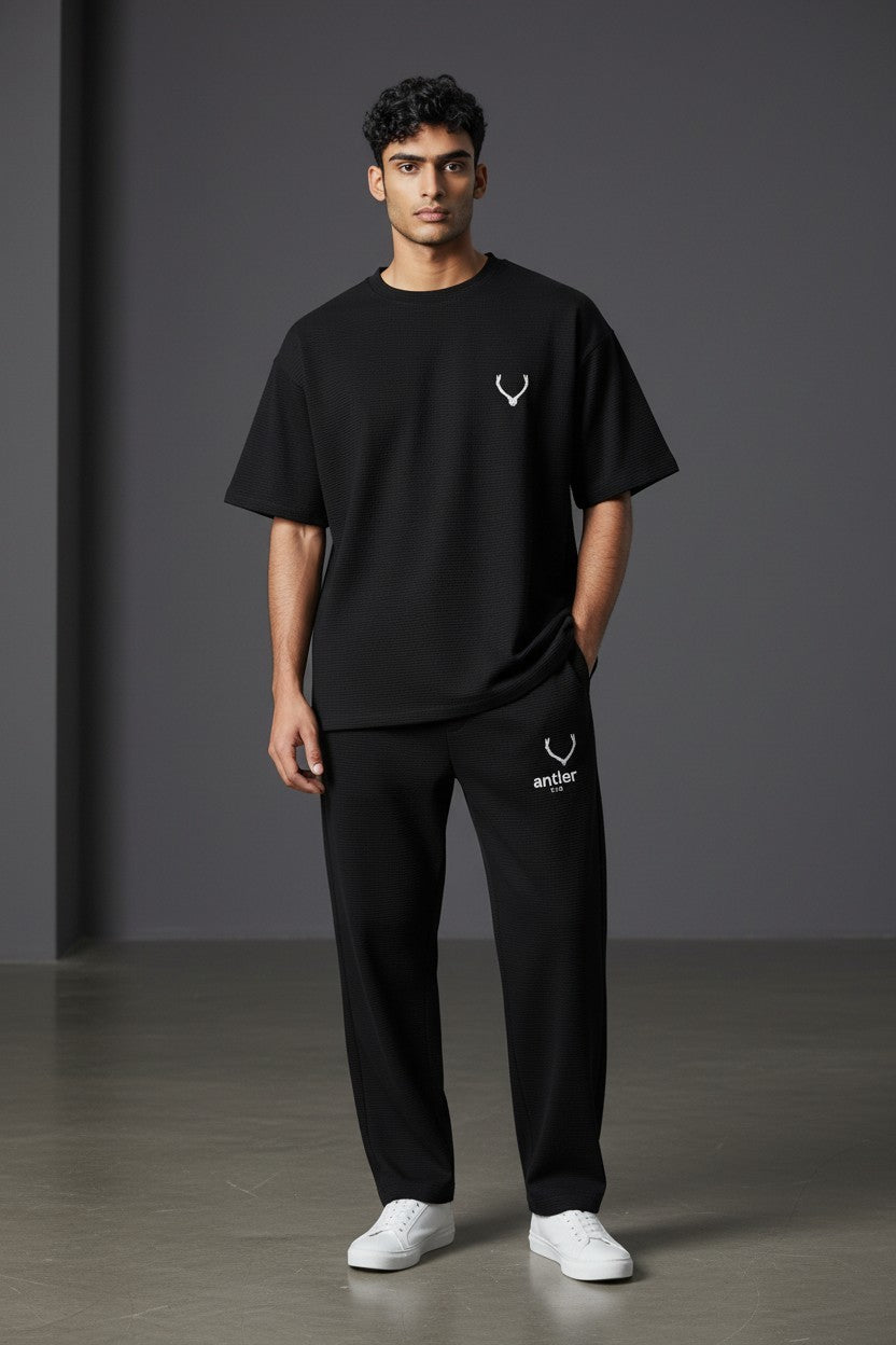 Person wearing a black t-shirt and pants with a logo on a gray background. Antler, Monza Outlet, Monza Fashion, Shein Outlet