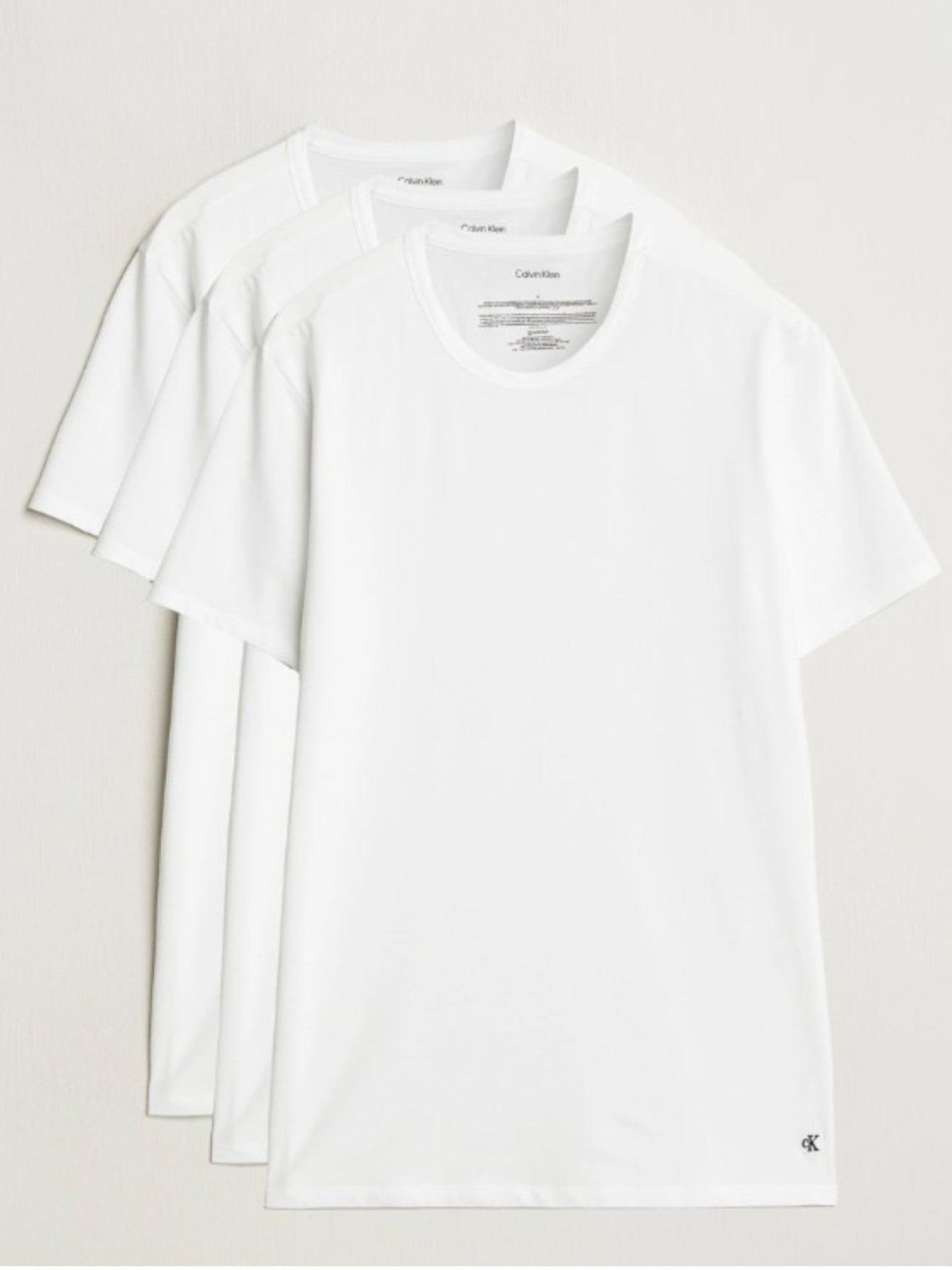 Three white short-sleeve crewneck tshirts from Calvin Klein, stacked neatly on a light beige background. Calvin Klein, Monza Outlet, Monza Fashion, Shein Outlet