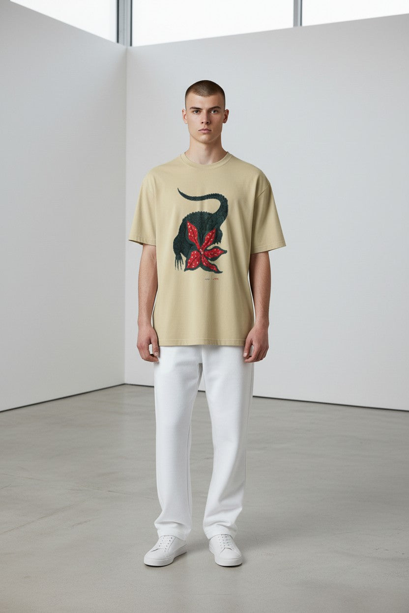 Man wearing a beige t-shirt with a graphic design in a minimalistic setting. Lacoste, Monza Outlet, Monza Fashion, Shein Outlet