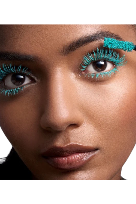 Woman applying turquoise eyelashes with a brush on a white background. Pat McGrath Labs Monza Outlet