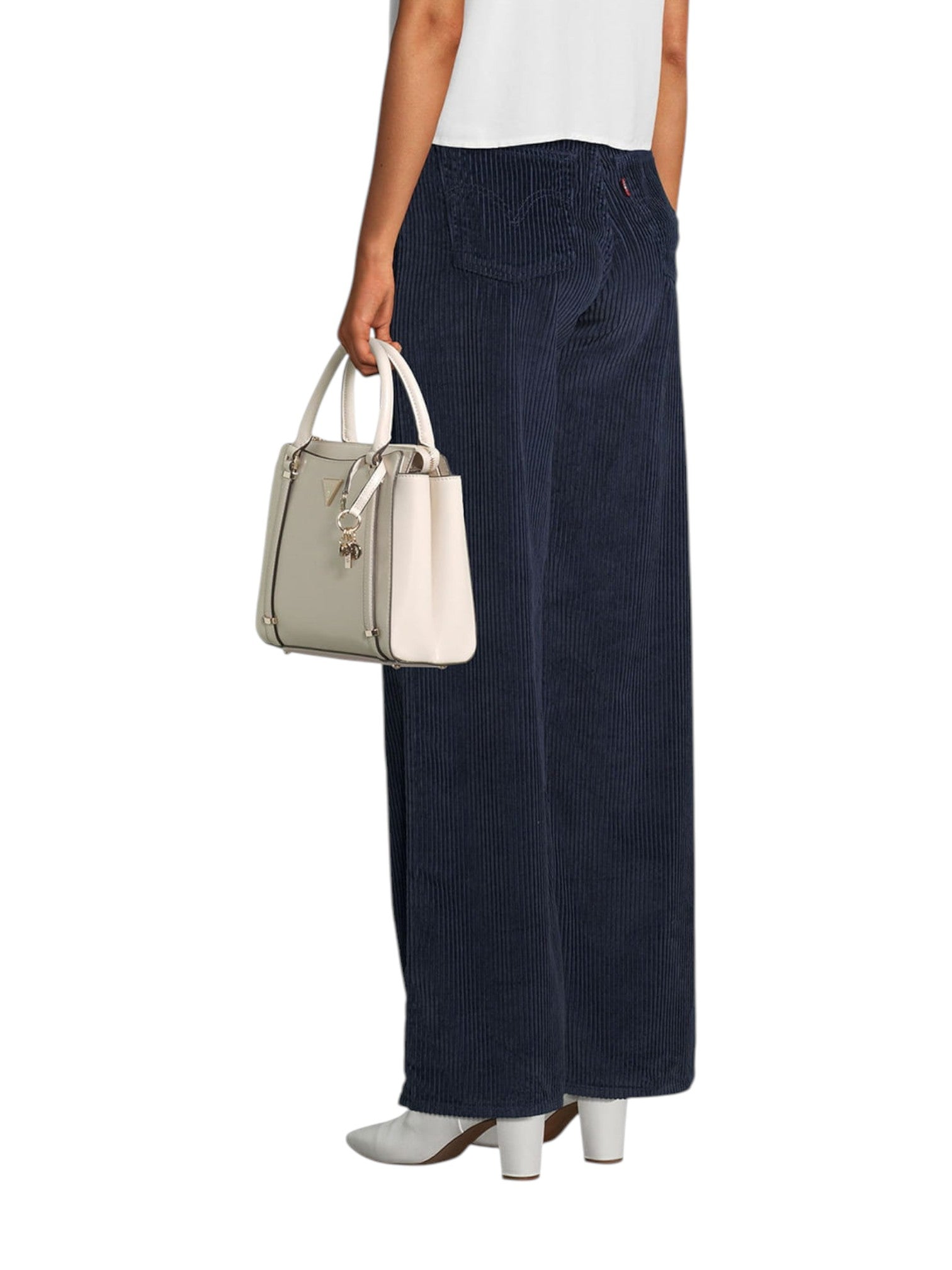 Person wearing navy corduroy pants holding a beige handbag on a white background. Guess, Monza Outlet, Monza Fashion, Shein Outlet