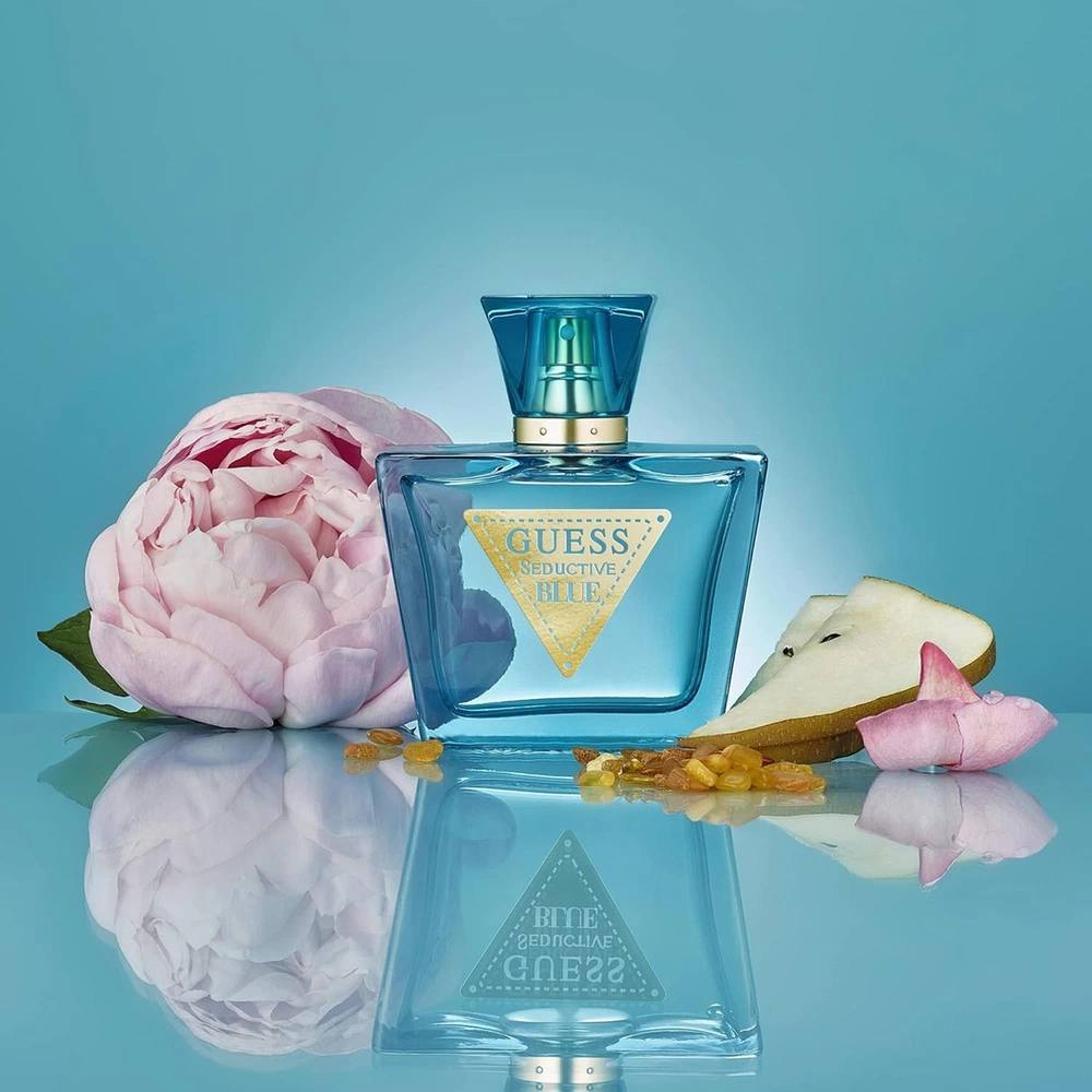 Blue Guess perfume bottle with a pink flower and seashell on a blue background Guess Monza Outlet
