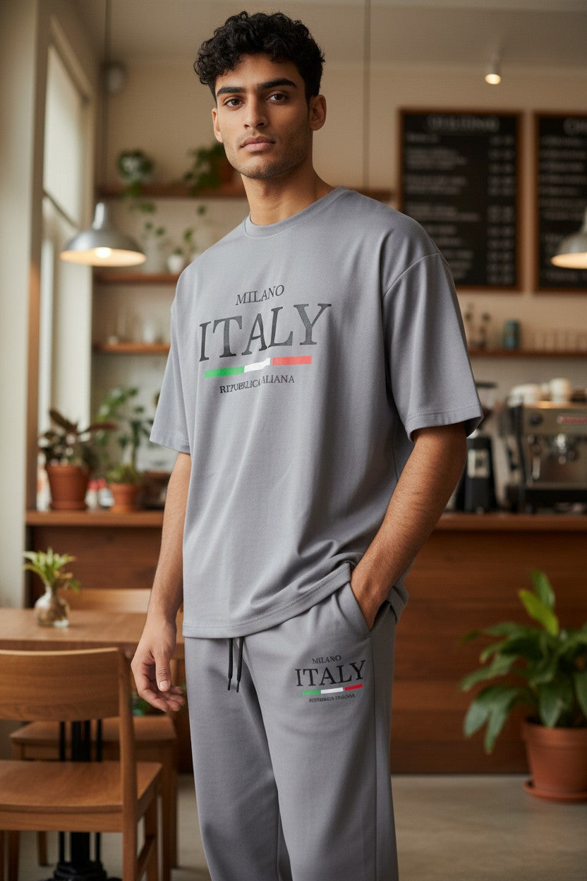 Man wearing a gray Milano Italy t-shirt and pants in a casual setting. Antler, Monza Outlet, Monza Fashion, Shein Outlet