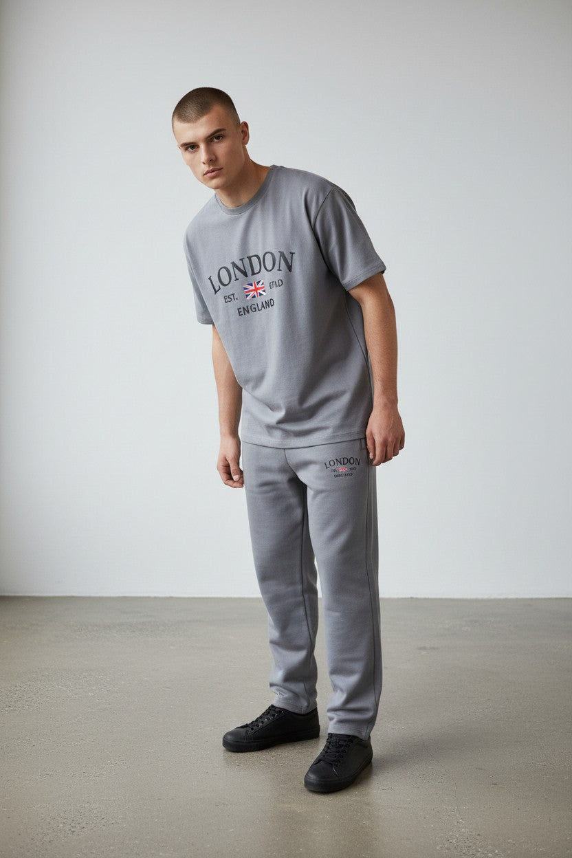 Man wearing a gray London t-shirt and pants against a white wall. Antler, Monza Outlet, Monza Fashion, Shein Outlet