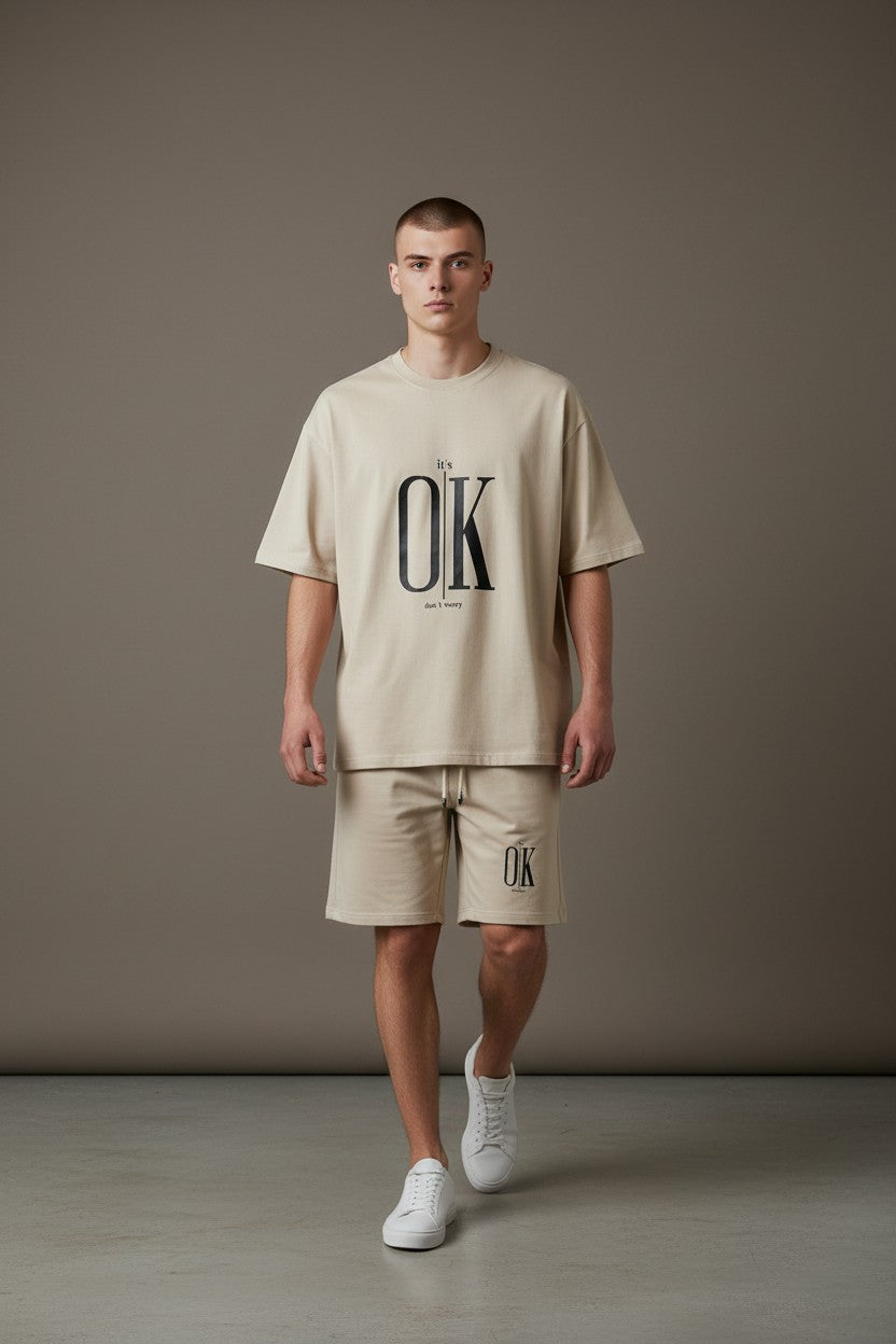 Man wearing a beige t-shirt and shorts with OK logo against a plain background. Antler, Monza Outlet, Monza Fashion, Shein Outlet
