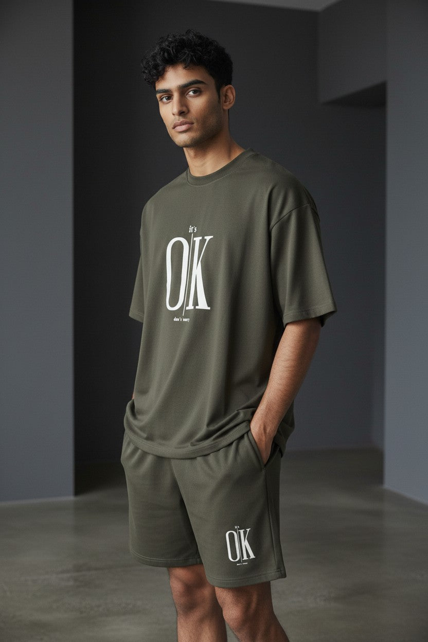 Man wearing a green t-shirt and shorts with OK logo in a minimalistic setting. Antler, Monza Outlet, Monza Fashion, Shein Outlet