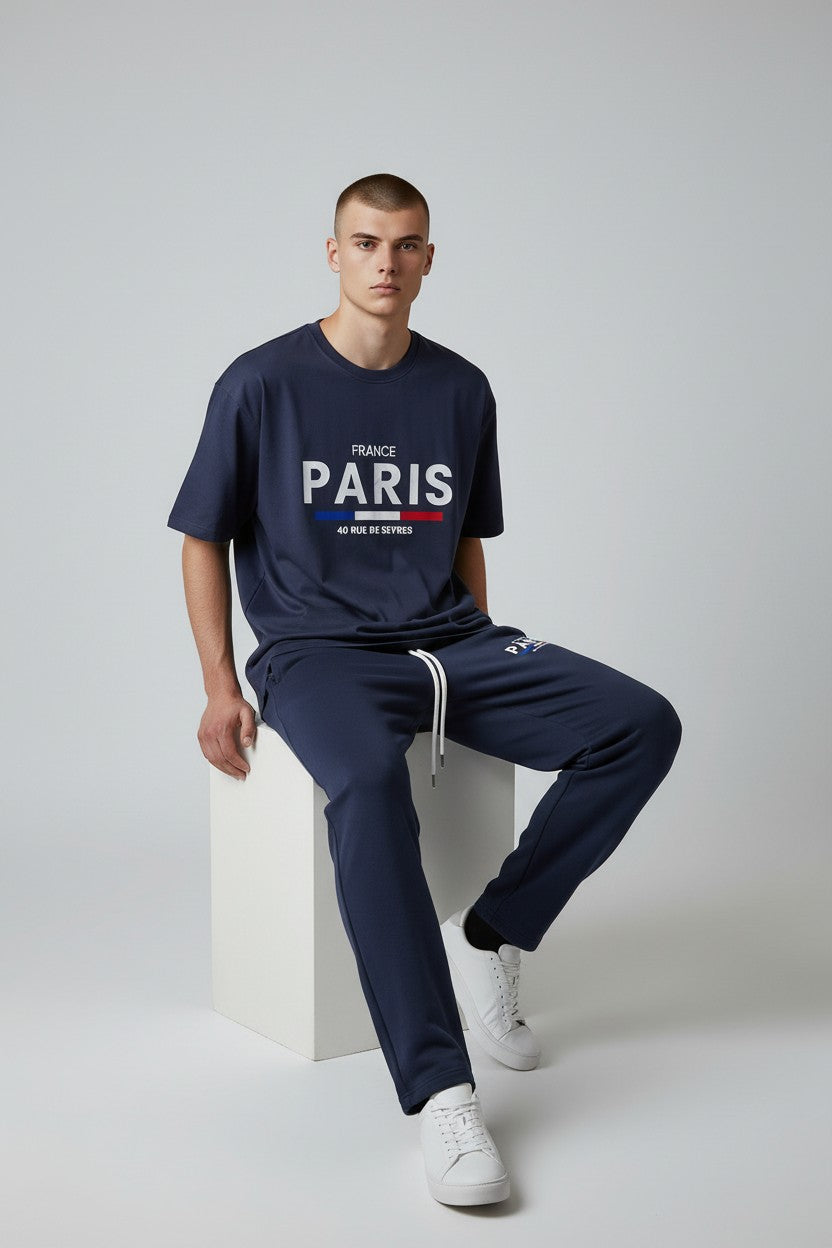 Man wearing a navy Paris t-shirt and pants sitting on a white block against a light gray background. Antler, Monza Outlet, Monza Fashion, Shein Outlet