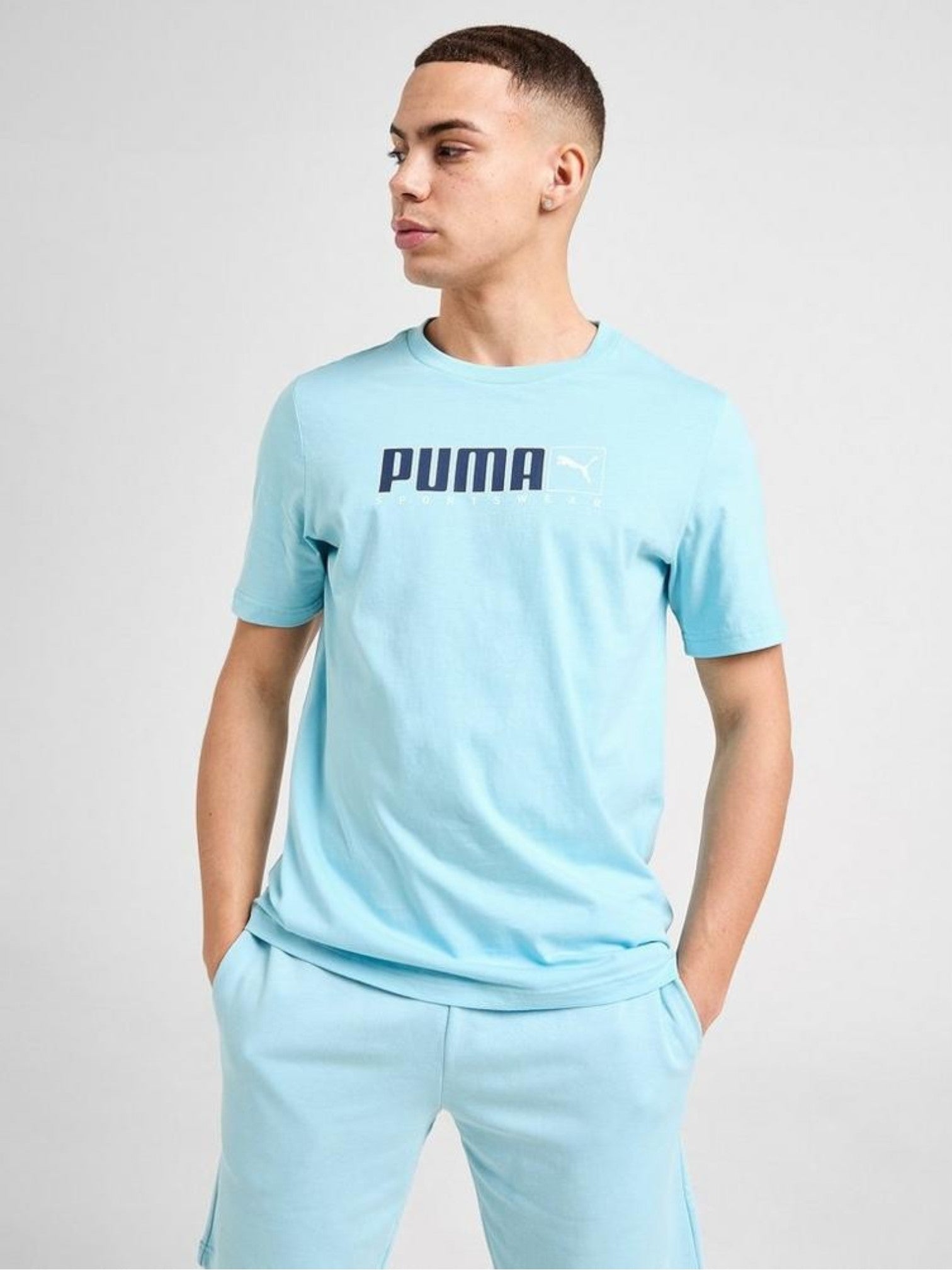 Person wearing a light blue Puma t-shirt and pants on a plain background. Puma, Monza Outlet, Monza Fashion, Shein Outlet