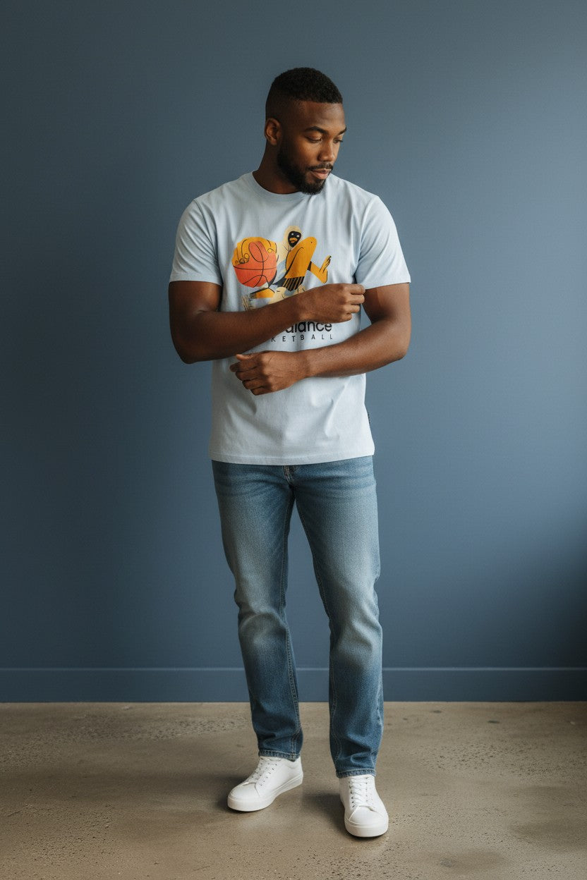 Man wearing a white t-shirt with a graphic design, blue jeans, and white sneakers against a gray wall. New Balance, Monza Outlet, Monza Fashion, Shein Outlet