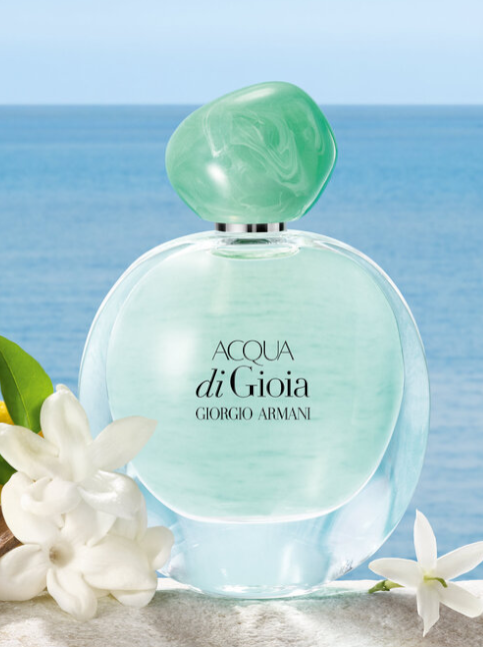 Perfume bottle of Acqua di Gioia by Giorgio Armani with flowers on a beach background. Monza Outlet