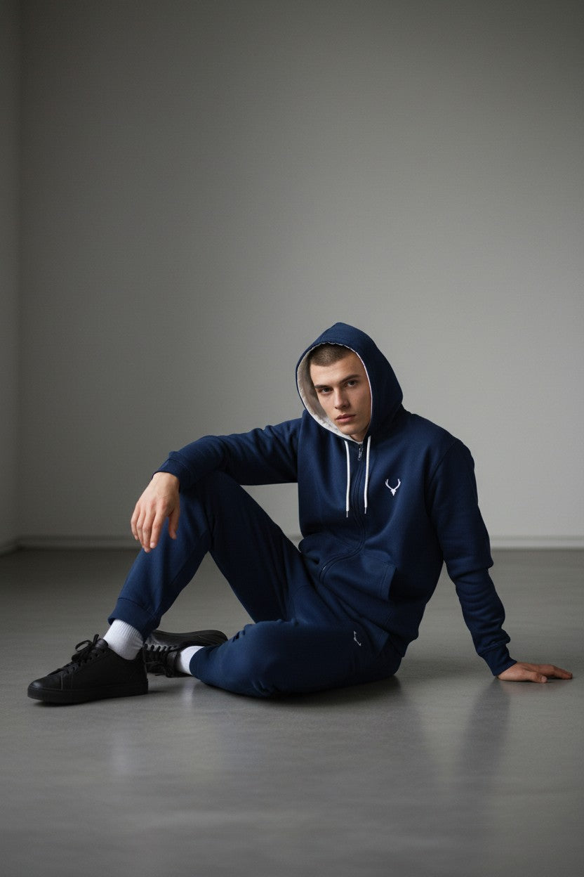 Person wearing a blue hoodie and pants sitting on the floor against a gray background. Antler, Monza Outlet, Monza Fashion, Shein Outlet